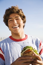 Smiling teen boy holding a sandwich