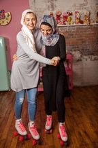 Two girls on roller skates, holing onto each other, having fun