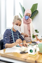 Young woman wearing face mask standing by coworker while working at office