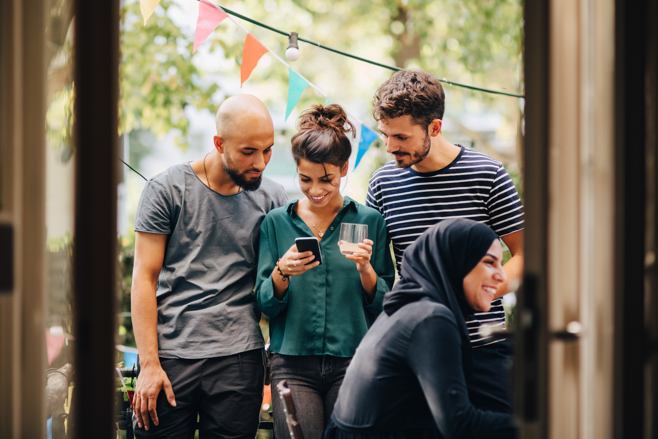 Smiling young woman showing mobile phone to male friends while standing in balcony during party
