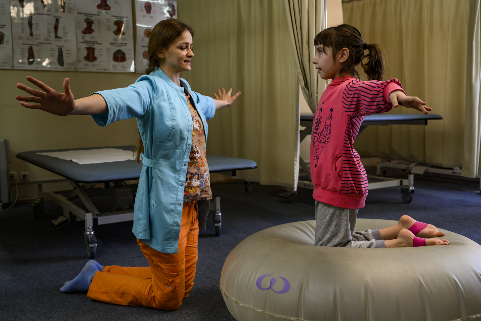 A child opens her arms as she kneels on a cushion, with a physical rehabilitation therapist for better coordination and balance, in Russia