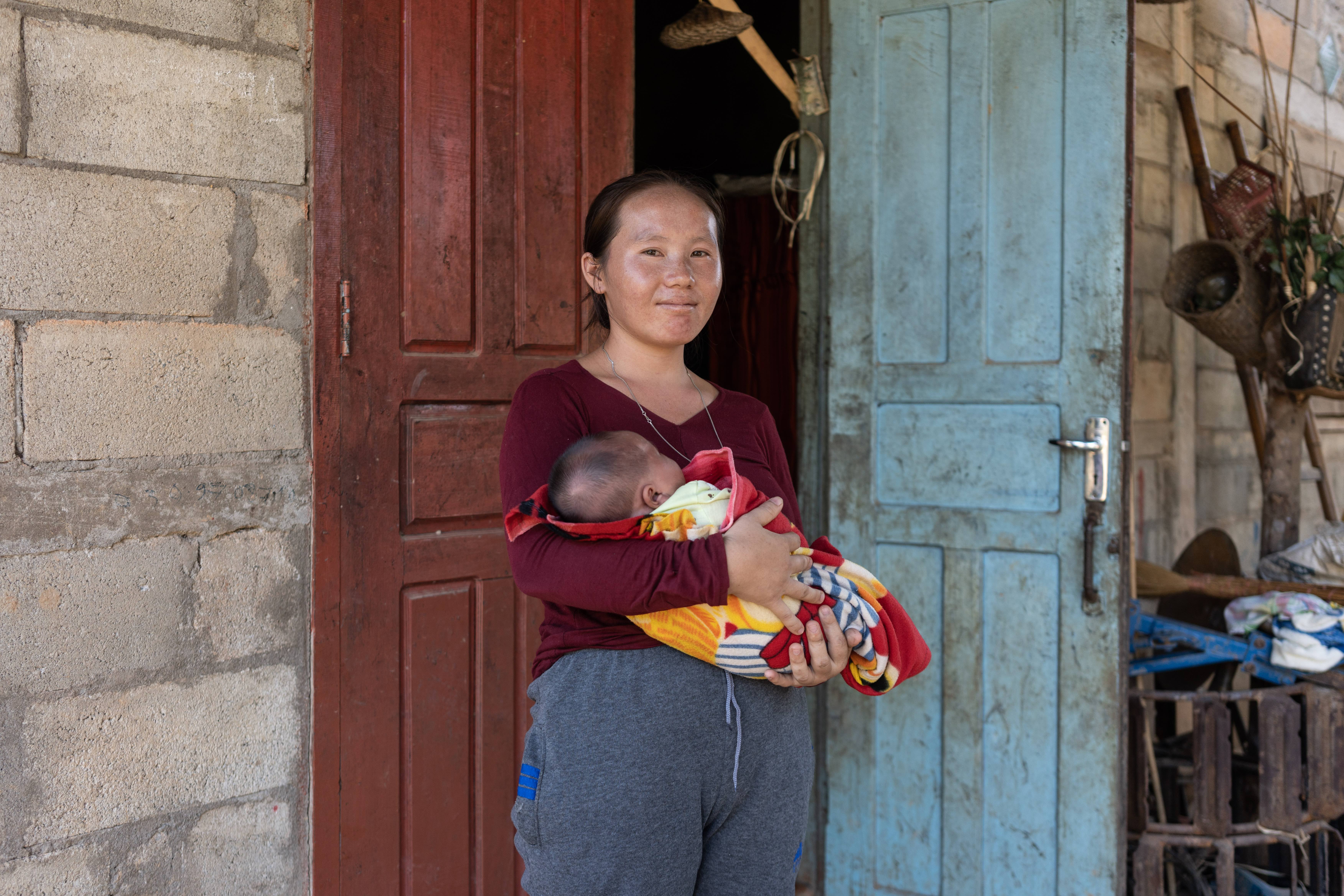 A mother holding her newborn baby in front of her house, in Lao People's Democratic Republic