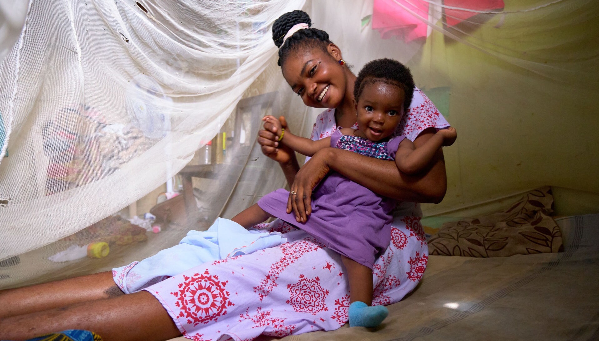 A mother and her daughter smiling under a mosquito net, in Ghana