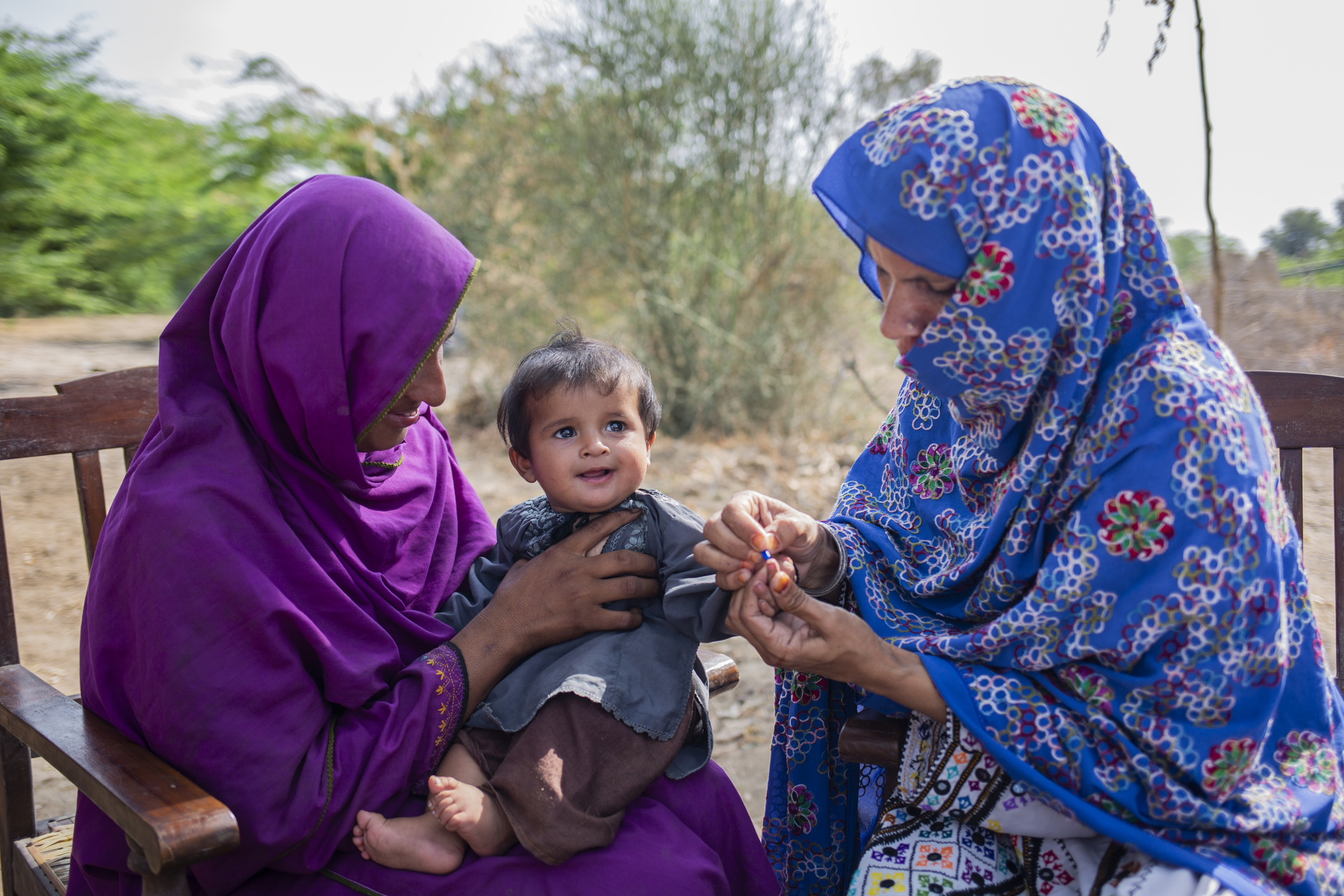 6-month-old baby gets tested for malaria by two women health workers in Naseerabad, Pakistan