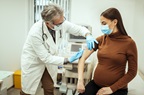 Pregnant woman getting vaccinated against flu or coronavirus. Male doctor giving an injection to pregnant patient while wearing face masks in the clinic.