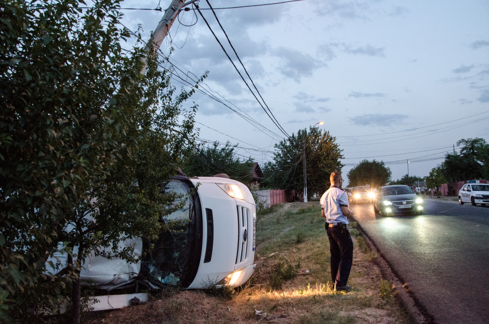 A vehicle is off the road and lying on its side; police are present at the scene, in Romaniaro