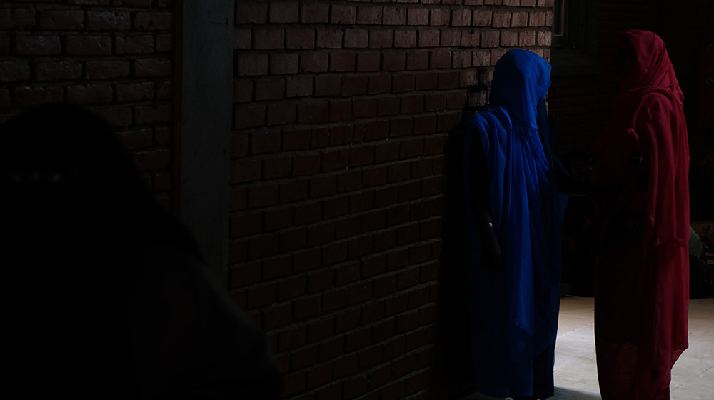 Two women in Sudan facing a wall, where their faces are not visible