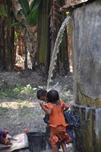 Children bathing under water coming out of a container, in Timor-Leste