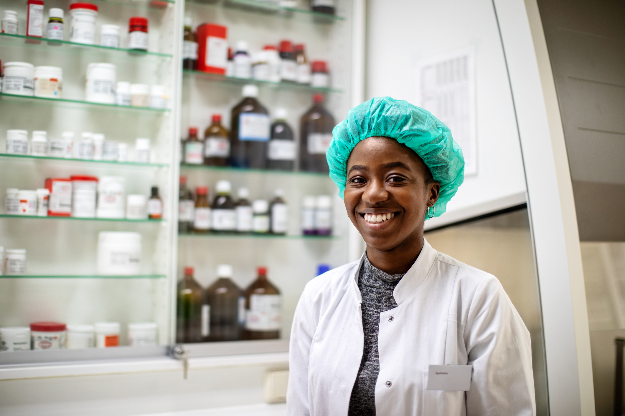 Portrait of a female chemist in lab coat with a protective cap in pharmacy