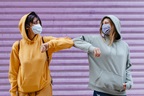 Two young women wearing masks greeting with elbow